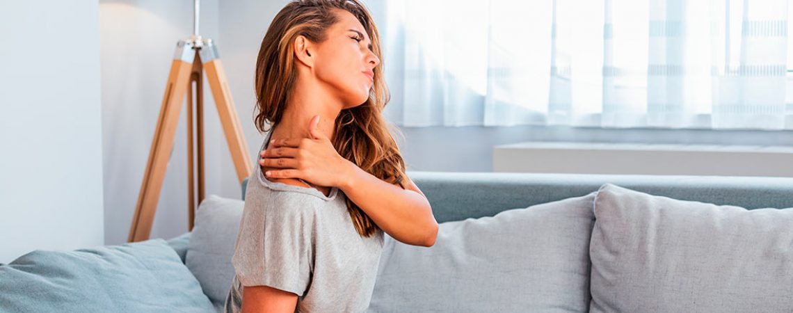 Mujer joven en el sofá con dolor de hombro